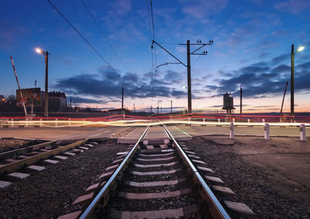 Rail crossing with blurred car lights at beautiful sunset. Railw