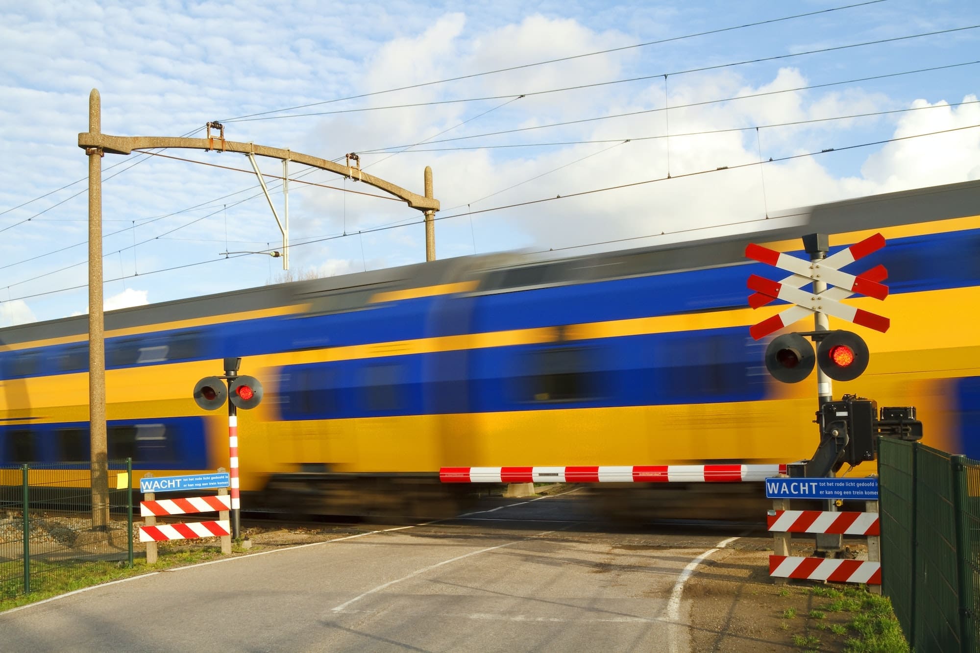 Dutch NS blue and yellow intercity express train passing railway crossing at high speed.